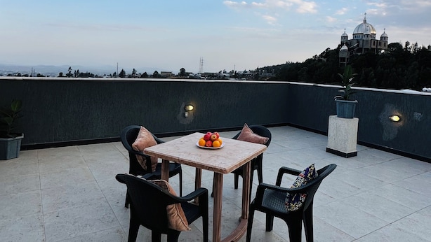 Una terraza en la azotea con una mesa, sillas, una planta en maceta y vistas a un edificio lejano.