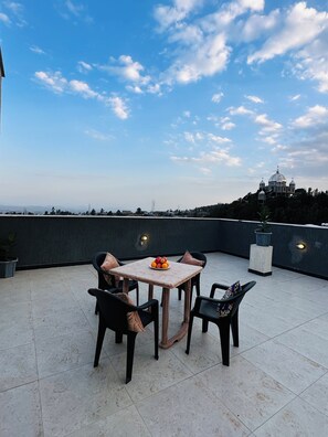A rooftop terrace with a table and chairs, a potted plant, and a view of a distant building.