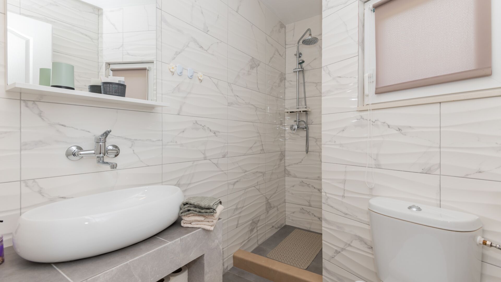 A bathroom with a white sink, marble walls, a shower, and a toilet.