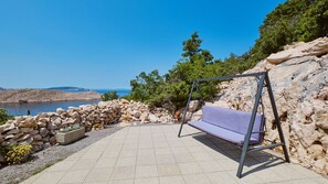 Eine Terrasse mit einer Schaukel, einer Steinmauer und Blick auf ein Gewässer.