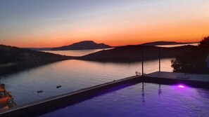 Blick auf den Sonnenuntergang von einer Poolanlage mit Wasseroberfläche und fernen Hügeln.