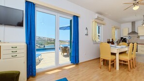 Ein Zimmer mit Esstisch, Stühlen, Fernseher und Meerblick durch große Fenster.
