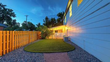 A backyard with a wooden fence, a lawn, and a house with string lights.