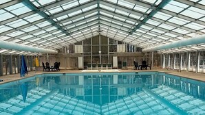 An indoor swimming pool with a glass ceiling, surrounded by chairs and a clock on the wall. - Private 6-Acre Retreat | Views, Hot Tub, Fire Pit (Ellijay)