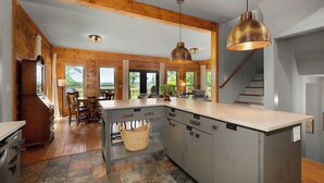 A modern kitchen with a large island, wooden beams, and large windows. - Private 6-Acre Retreat | Views, Hot Tub, Fire Pit (Ellijay)