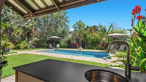 A poolside area with a built-in sink, lounge chairs, and umbrellas. - Tropic Bliss l Pool Oasis l Mins to DNTN (St. Augustine)