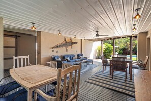 Un espace extérieur aménagé en terrasse, avec une table et des chaises en bois, un ensemble de canapés bleus et un ventilateur de plafond.