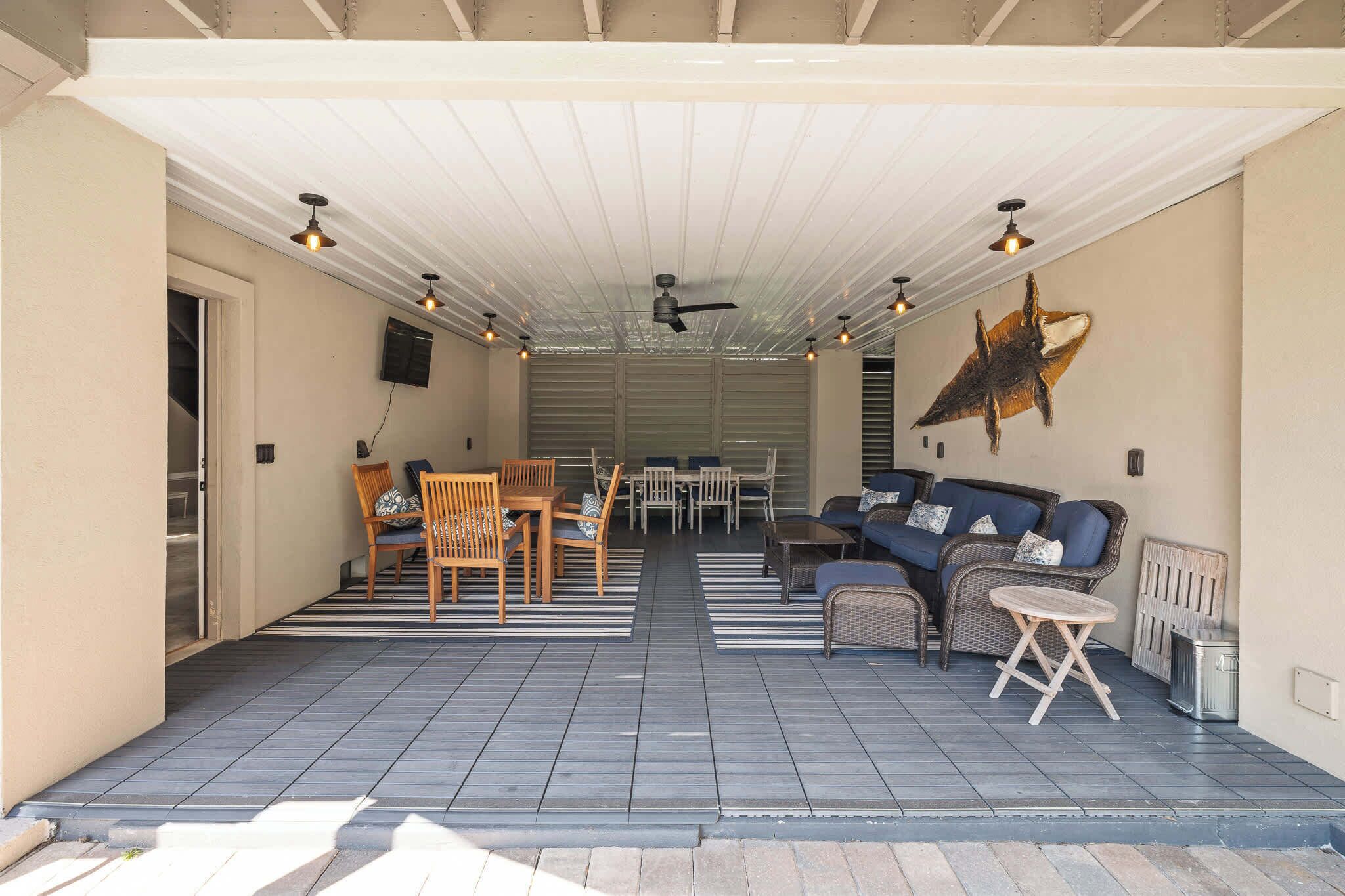Een overdekt terras met een plafondventilator, zitgedeelte met een bank en stoelen, en een decoratief muurdecoratie.