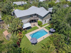 Une grande maison avec une piscine, entourée d’une végétation luxuriante et de palmiers.