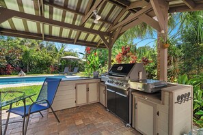 Une cuisine extérieure équipée d’un barbecue, d’un évier et d’une chaise.