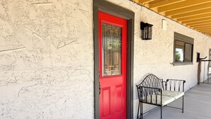 A red door with a window, a bench, and a wall with a textured surface.