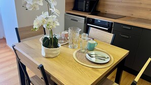 A dining area with a wooden table, chairs, a vase of white orchids, a pitcher, glasses, and a microwave above the cabinets. - Villa Anita -town center -private parking- wifi. (Barcelonnette)