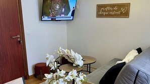 A living room with a wooden dining table, a TV mounted on the wall, a sofa, and a decorative sign. - Villa Anita -town center -private parking- wifi. (Barcelonnette)