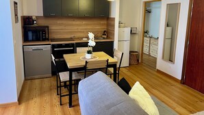 A compact kitchen with modern appliances, a dining area with a table and chairs, and a sofa in the living space. - Villa Anita -town center -private parking- wifi. (Barcelonnette)