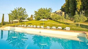 A swimming pool with lounge chairs and umbrellas, surrounded by trees and a building in the background. - Villa Rama: A splendid seventeenth-century two-story historical villa surrounded by meadows and by green hills, with Free WI-FI. (Gambassi Terme)
