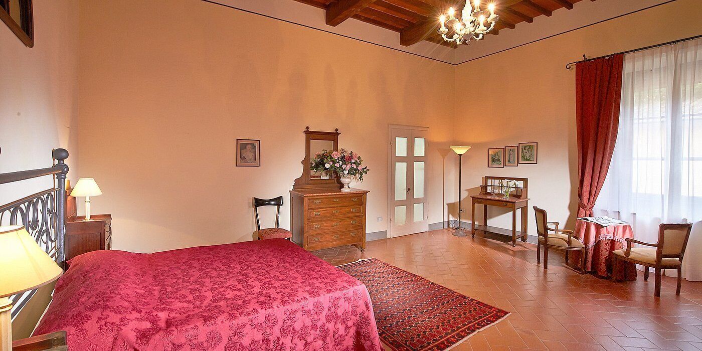 A bedroom with a bed, dresser, chair, table, and a window with curtains.