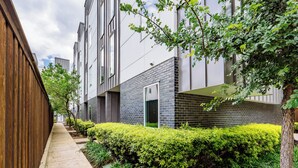 Een modern gebouw met een bakstenen gevel, een houten hek en verzorgde beplanting langs de stoep.