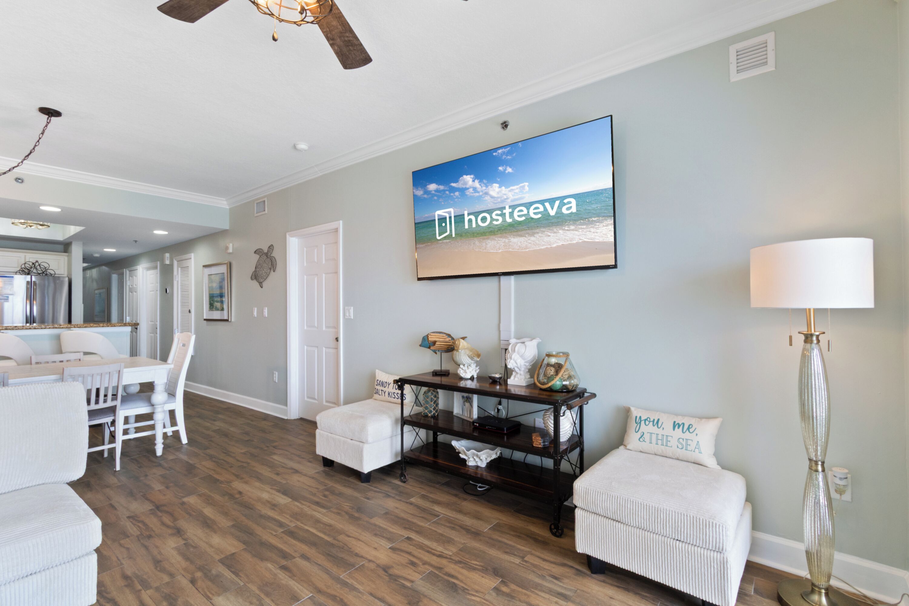 A spacious living room with a dining area, a television mounted on the wall, and a lamp.