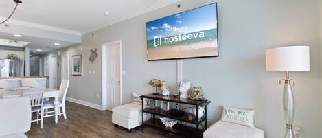 A spacious living room with a dining area, a television mounted on the wall, and a lamp.