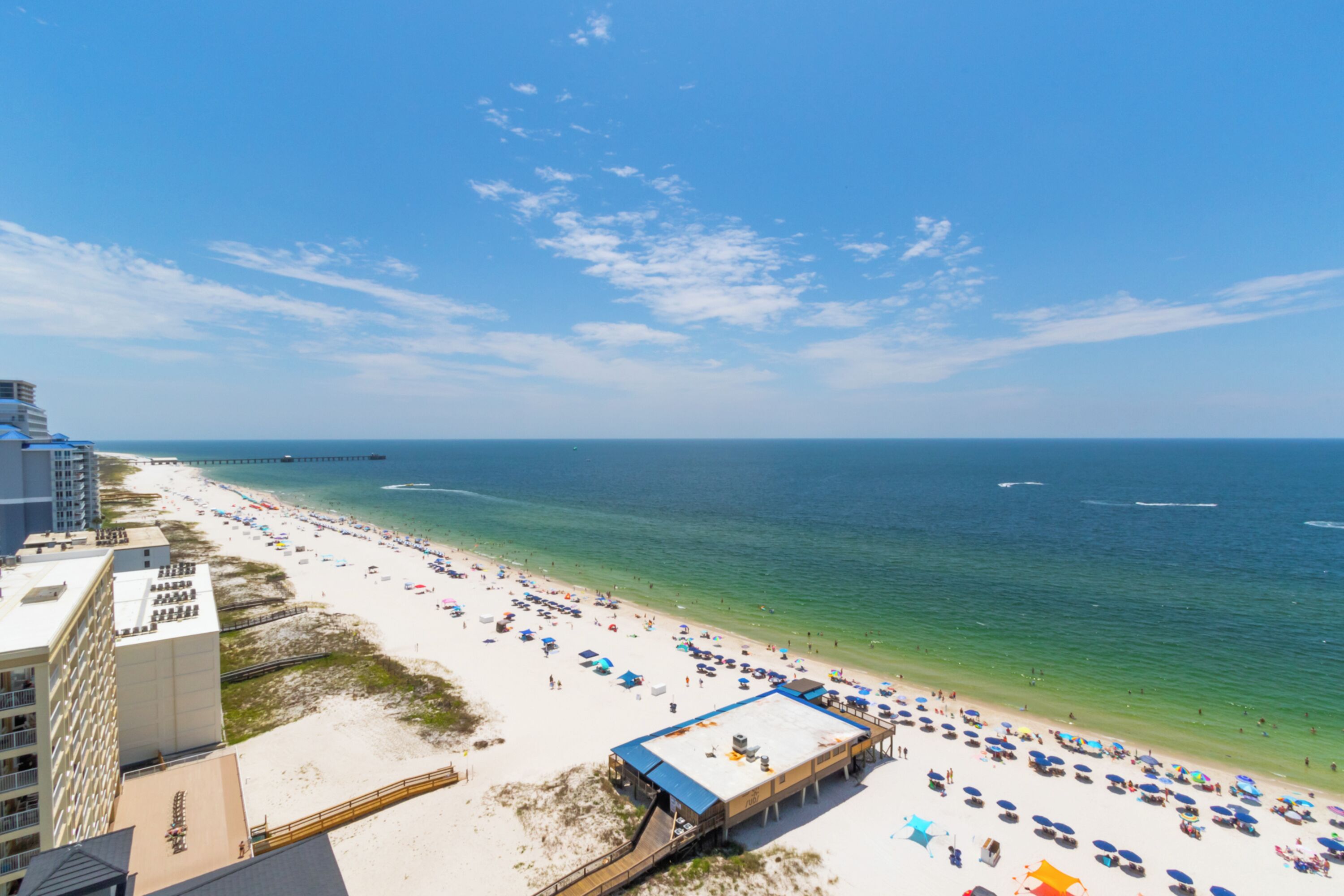 A beach with a pier, a hotel, and a beach umbrella area.