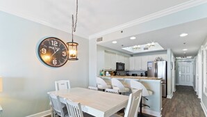 A modern kitchen with white cabinetry, a central island, and a dining area with a wooden table and white chairs. - Seawind 1502 (Gulf Shores)