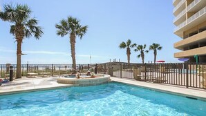 A swimming pool with a circular hot tub, surrounded by palm trees and a fence. - Seawind 1502 (Gulf Shores)