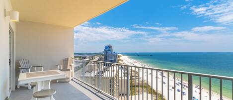 A balcony with a view of a beach, a dining table, and two chairs.
