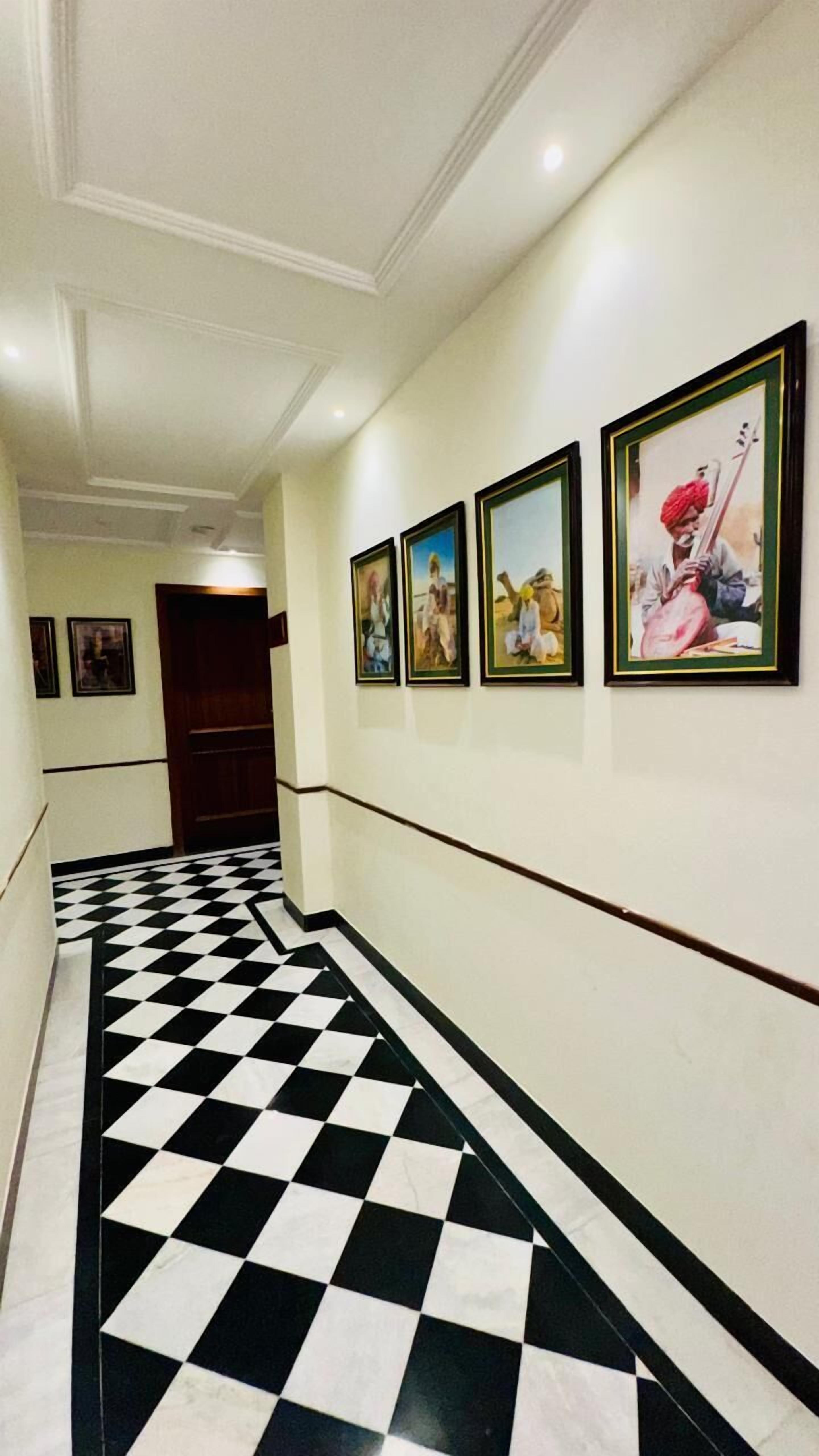 Un couloir avec un sol à carreaux noirs et blancs, des murs blancs et des tableaux encadrés accrochés au mur.