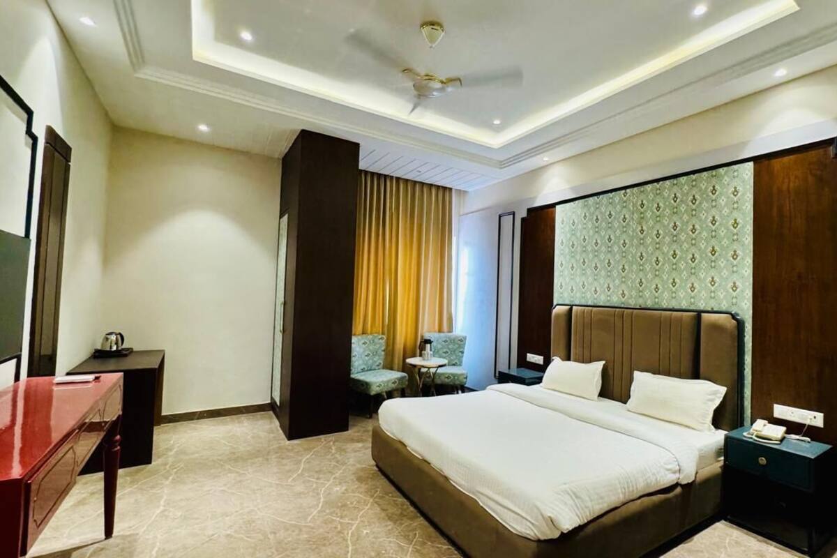 Habitación de hotel con una cama grande, un escritorio, una silla, una mesita pequeña y una mesita de noche.