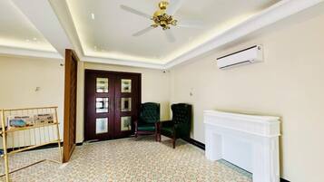 Habitación con ventilador de techo, radiador, dos sillas, puerta con paneles de vidrio y piso estampado.