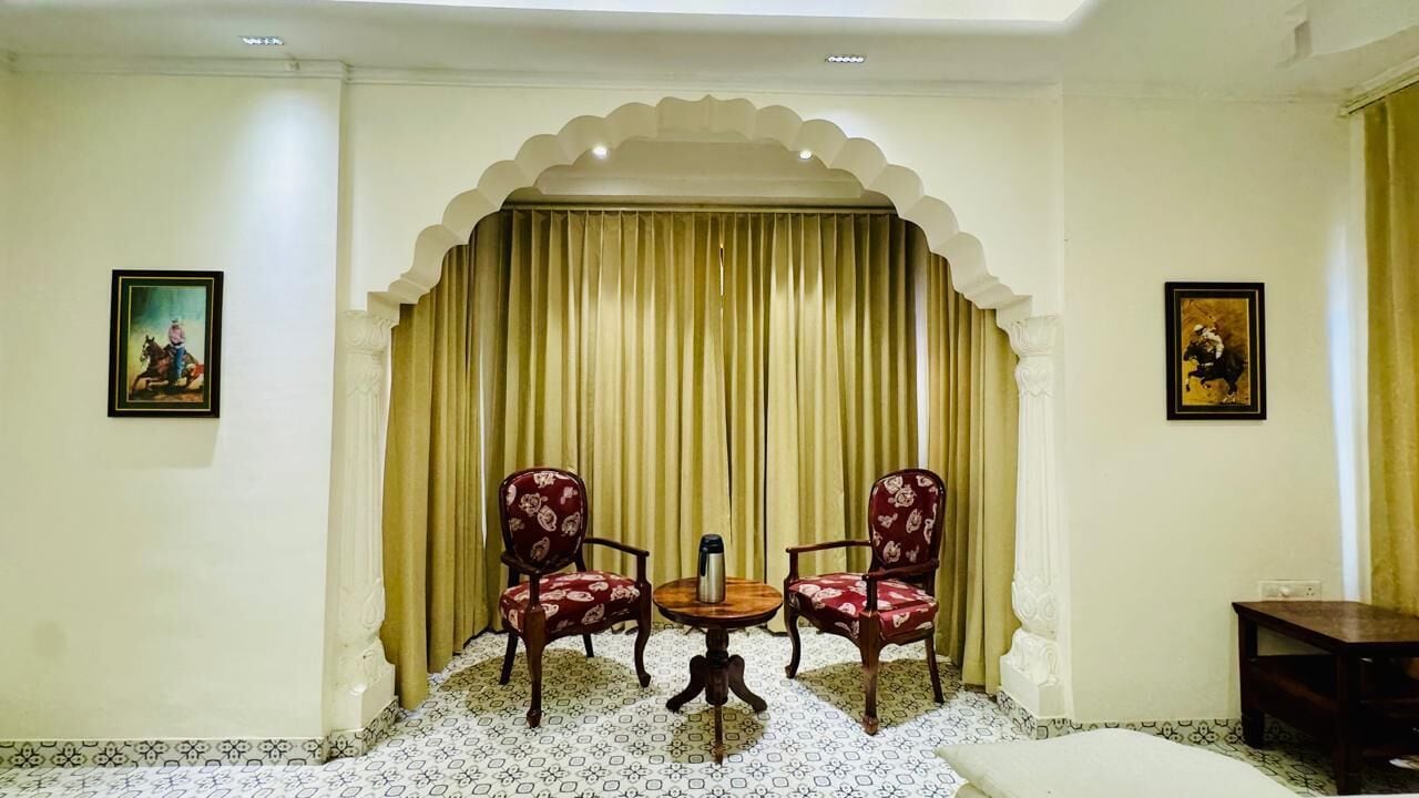 A room with a traditional design, featuring a patterned floor, a central table with chairs, and a decorative archway with curtains.