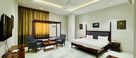 A hotel room with a four-poster bed, a television, a desk, and a chair.
