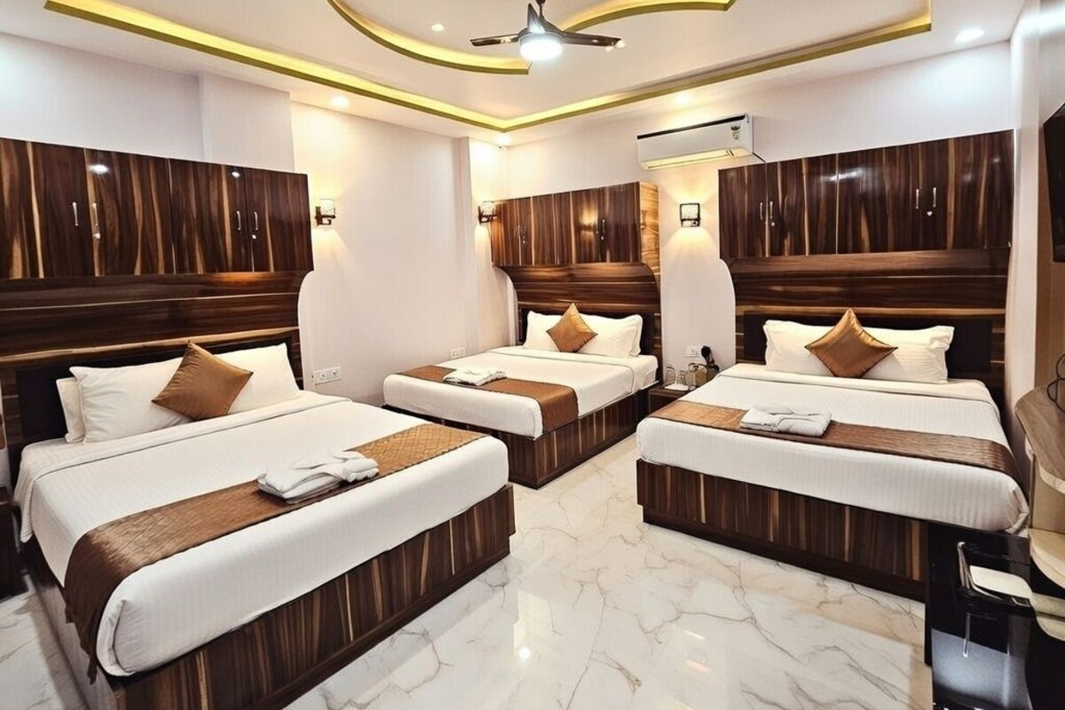 A hotel room with three beds, wooden headboards, marble flooring, and a ceiling fan.