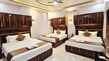 A hotel room with three beds, wooden headboards, marble flooring, and a ceiling fan.