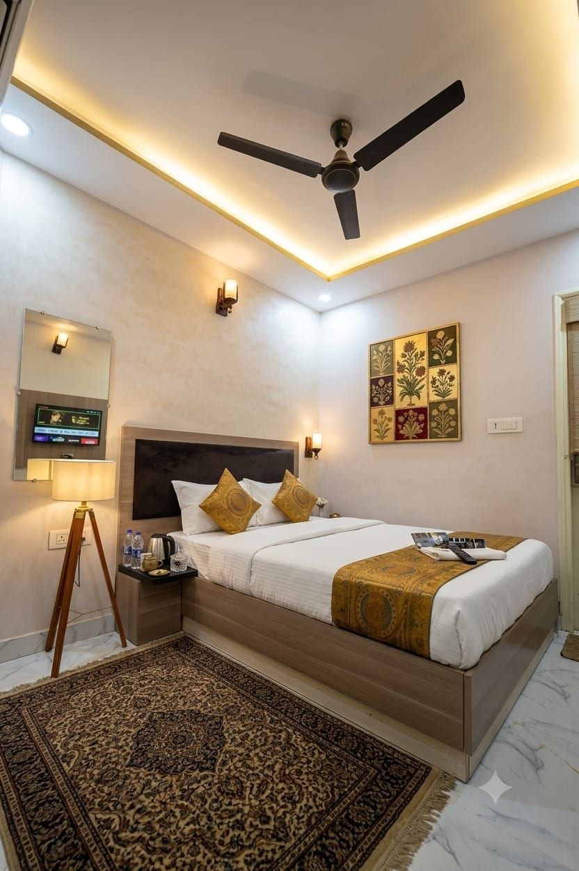 Habitación de hotel con cama, mesita de noche, lámpara, televisor montado en la pared y ventilador de techo, además de decoración en la pared.
