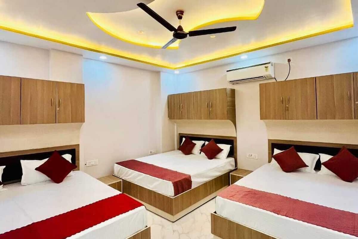 A hotel room with three beds, each with a wooden headboard and red bedding. The room has a modern ceiling design with recessed lighting and a ceiling fan.
