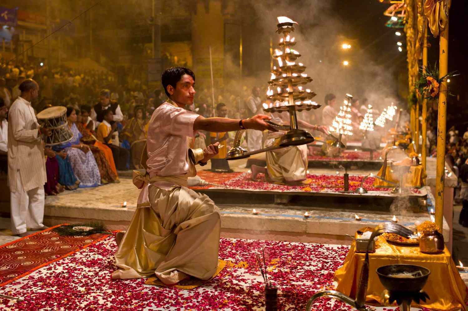 A person performing a ritual with a fire altar in a crowded temple setting.