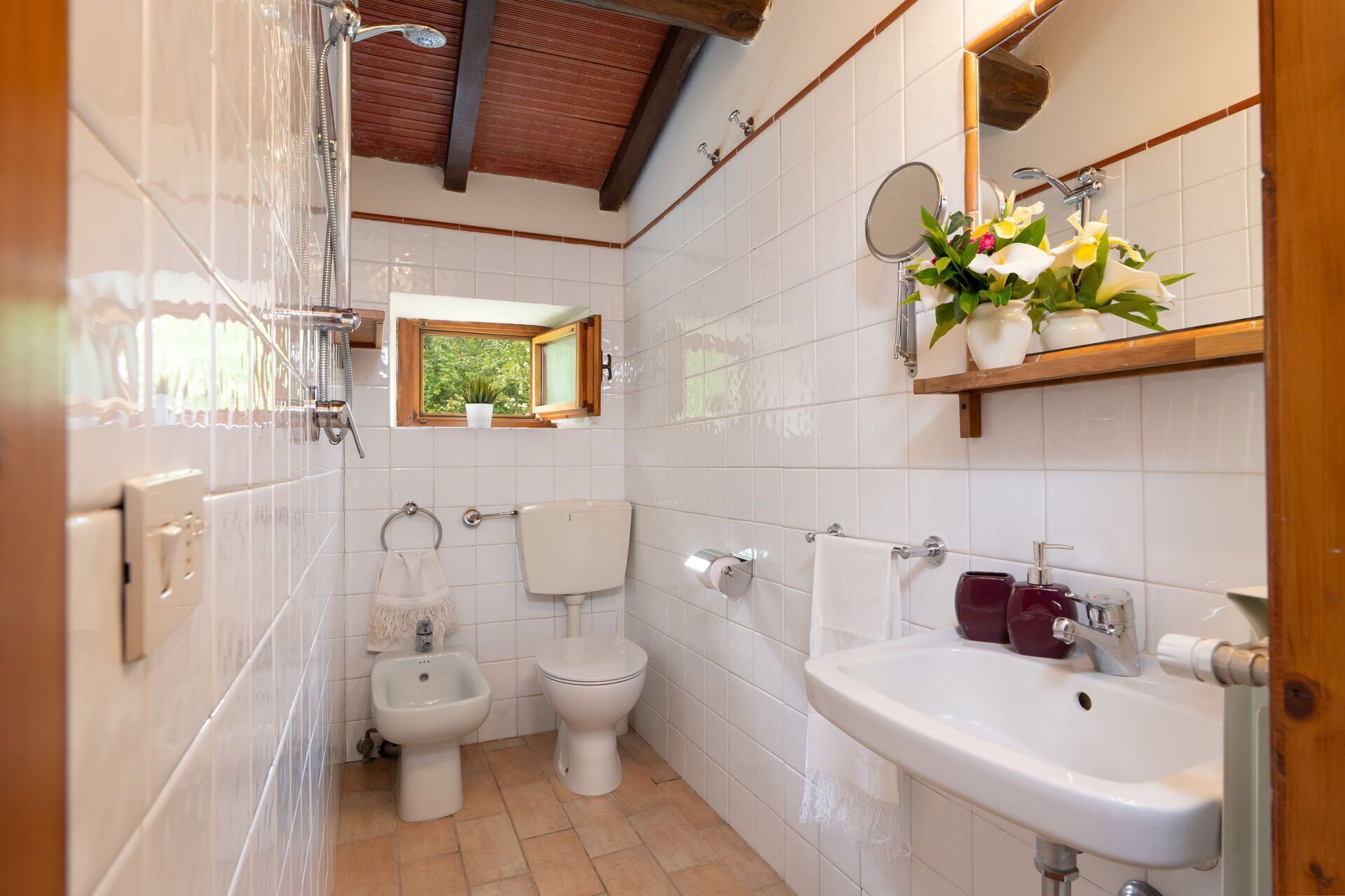 Une salle de bain avec douche, deux toilettes, un bidet, un lavabo et une fenêtre donnant sur un espace verdoyant.