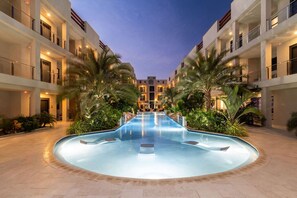 Un hotel con una piscina central rodeada de palmeras y un edificio de varios pisos con balcones.