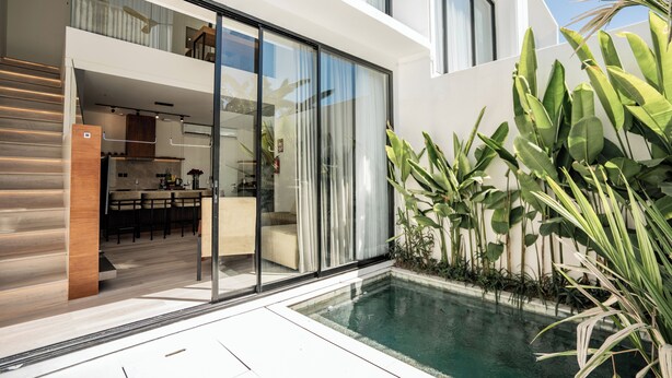 A modern house with a glass door leading to a kitchen, a pool, and a patio area with plants. - Charming 2-bedroom Oasis Smart Apartment with AC, WiFi in marvelous Bali (Bali)