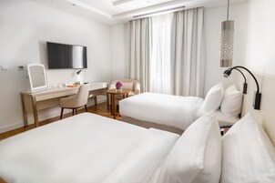 Habitación de hotel con dos camas, un escritorio, una silla, un televisor y una ventana con cortinas.