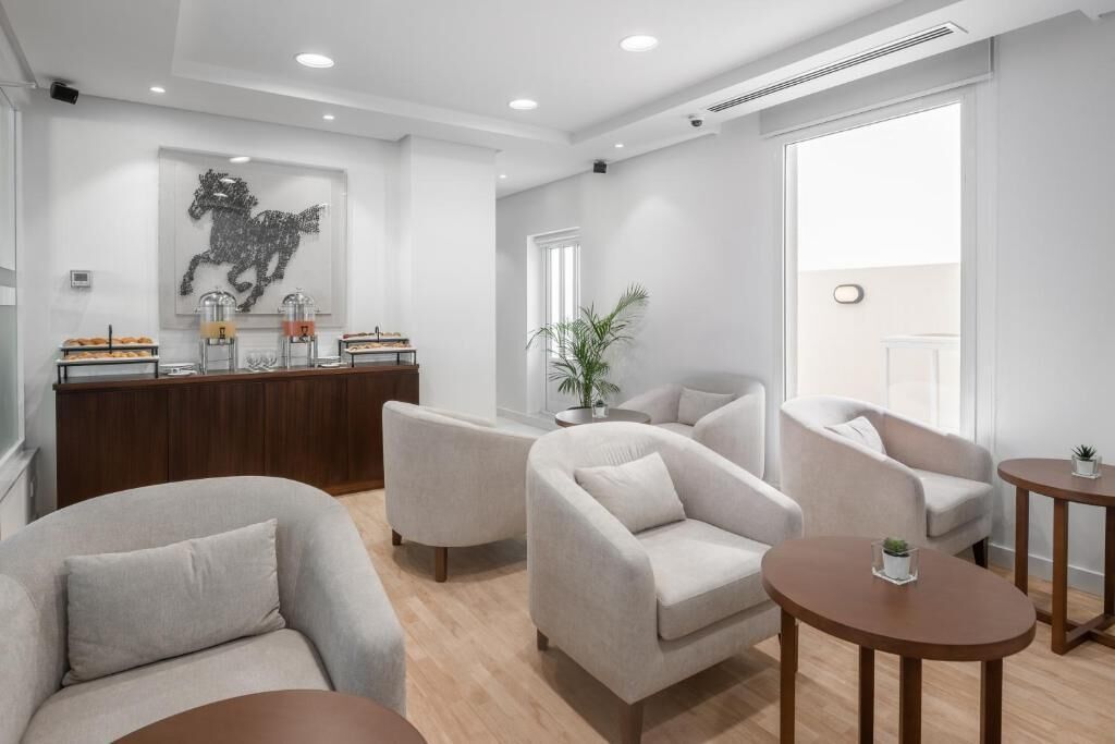 A modern hotel lobby with a reception desk, seating area, and a large window providing natural light.