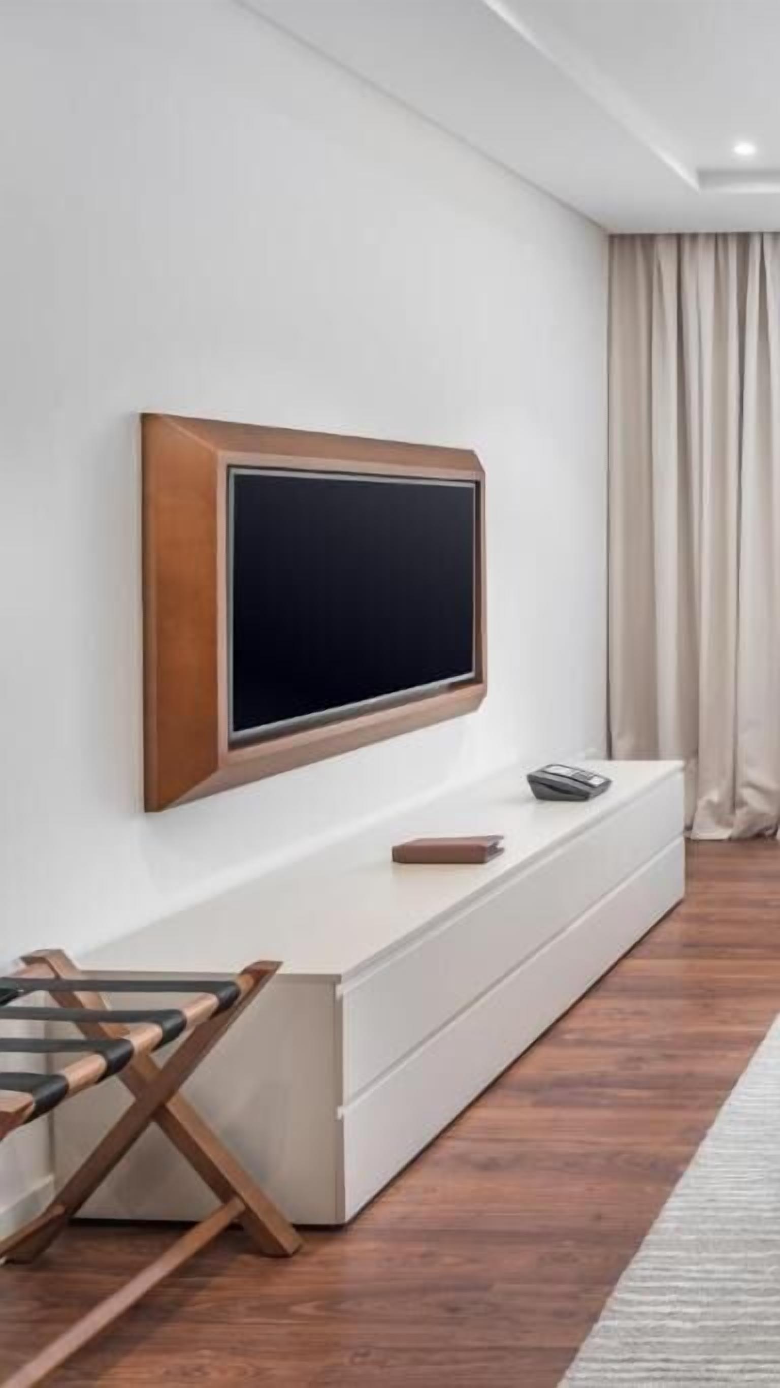 Ett modernt vardagsrum med en stor, platt-TV som är monterad på en vit vägg, ett vitt TV-bord under och ett trägolv.