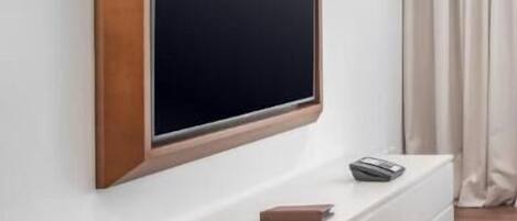 A modern living room with a large flat-screen TV mounted on a white wall, a white entertainment unit below, and a wooden floor.