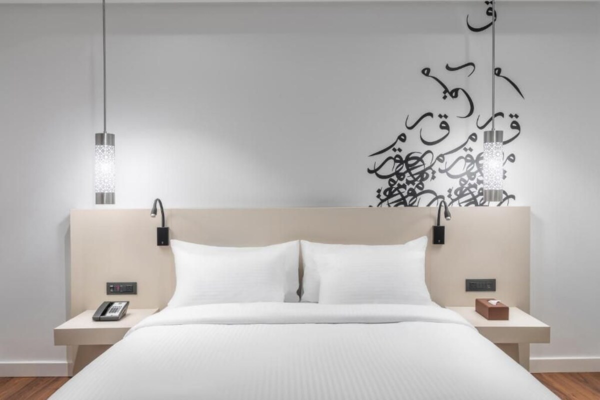 A modern hotel room with a bed, bedside tables, a phone, and a decorative wall piece.