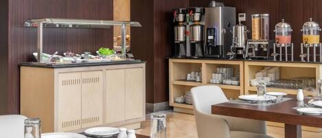 A modern hotel dining area with a buffet setup, including a coffee station and various food items.