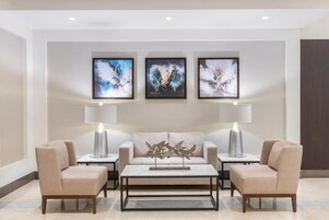 A modern living room with a sofa, two armchairs, a coffee table, and three framed artworks on the wall.