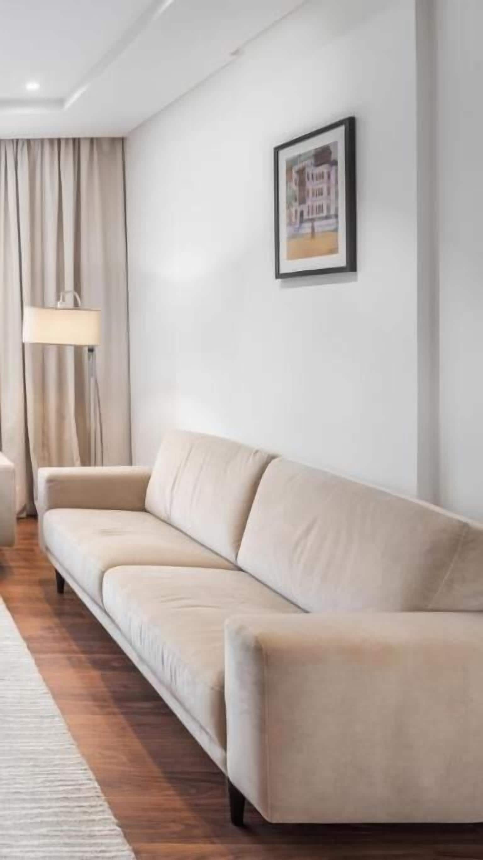 A modern living room with a beige sofa, a floor lamp, and a framed picture on the wall.