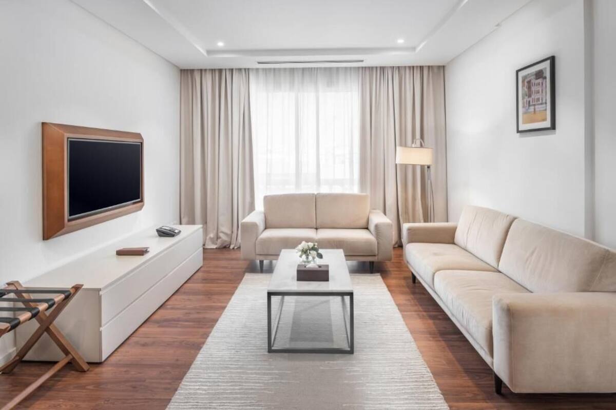 A modern living room with a flat-screen TV, two sofas, a coffee table, and a window with curtains.