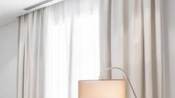 Una habitación de hotel moderna con un sofá beige, una lámpara de pie y cortinas de gasa.